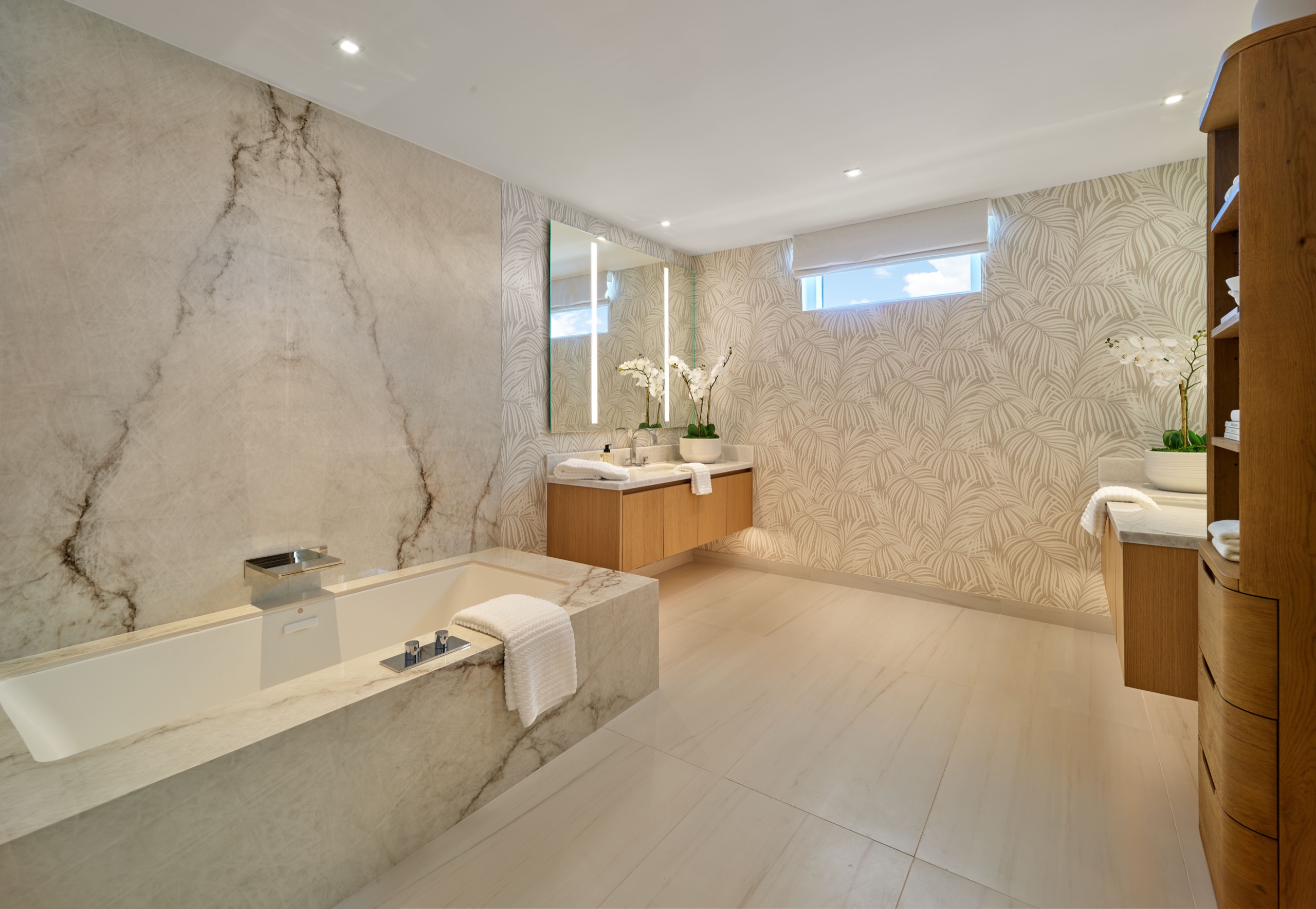 The primary bath as delivered: stone slab, palm wallpaper, twin oak vanities